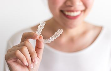 Nose-to-chest view of woman in white smiling holding Invisalign