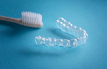 Toothbrush next to clear aligner on light blue surface